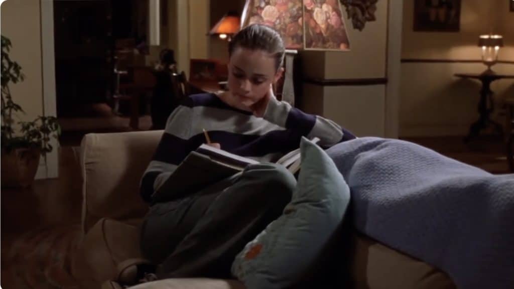 a photo of Rory gilmore sitting on the couch wearing a striped sweater and reading